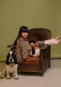 A young firl say sideways on an armchair with a cat, dog and rabbit next to her